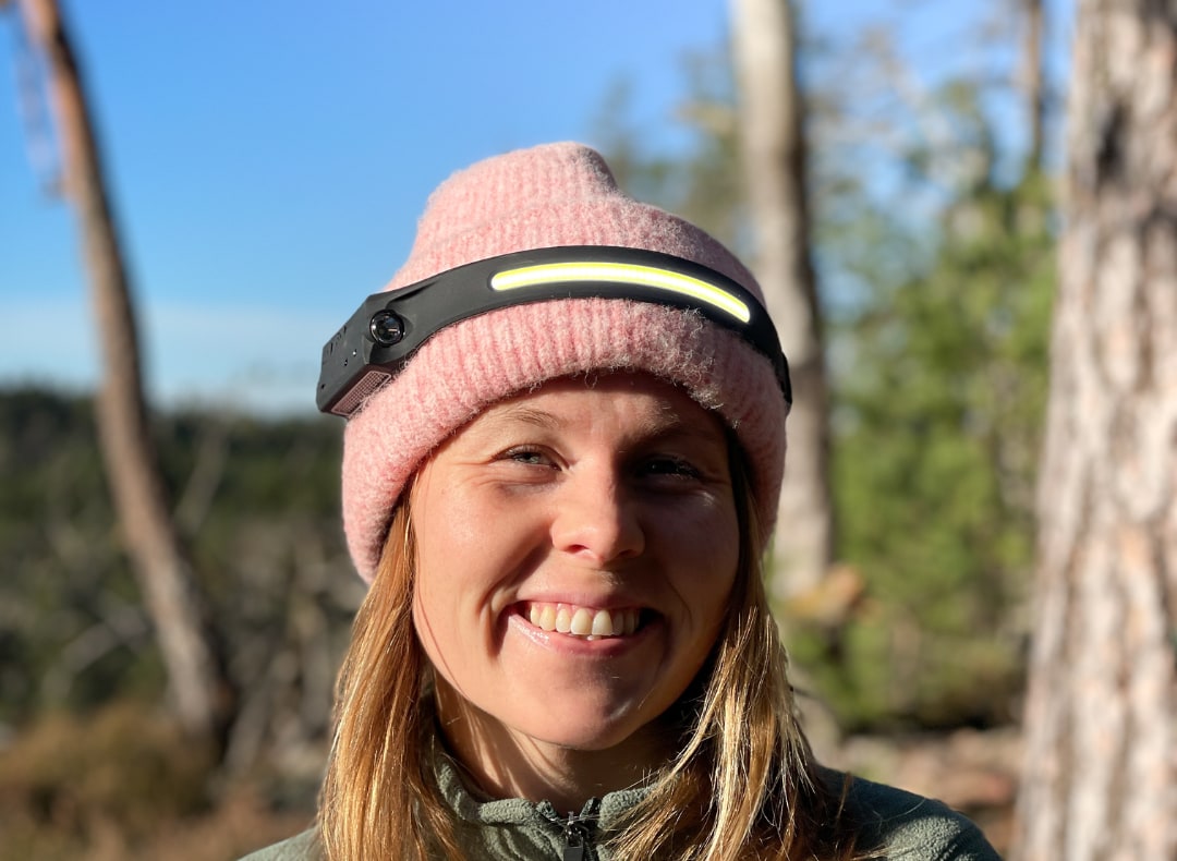 Kvinne med rosa lue og hodelykten over lua i skogen